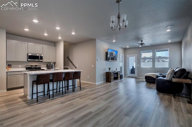 kitchen featuring stainless steel appliances, light countertops, hanging light fixtures, open floor plan, and a kitchen island with sink