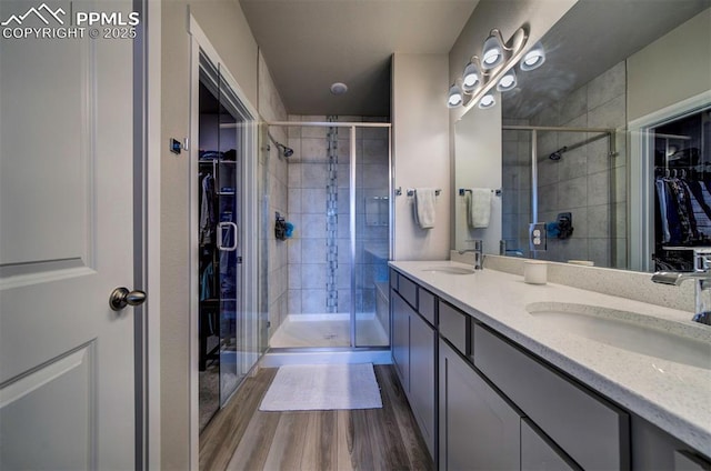 full bath with a walk in closet, a sink, a shower stall, and wood finished floors