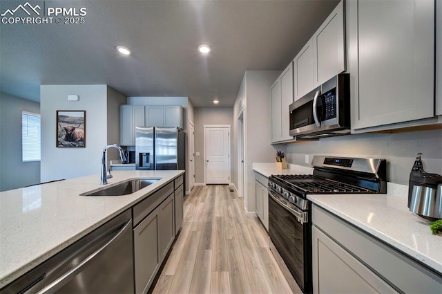 kitchen with light stone countertops, appliances with stainless steel finishes, sink, and light hardwood / wood-style flooring