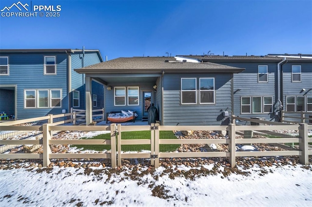 snow covered property with a fenced front yard and roof with shingles