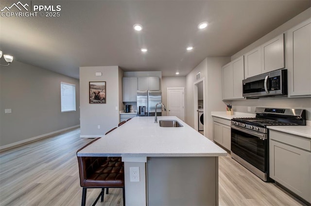 kitchen with appliances with stainless steel finishes, a sink, light wood finished floors, and an island with sink