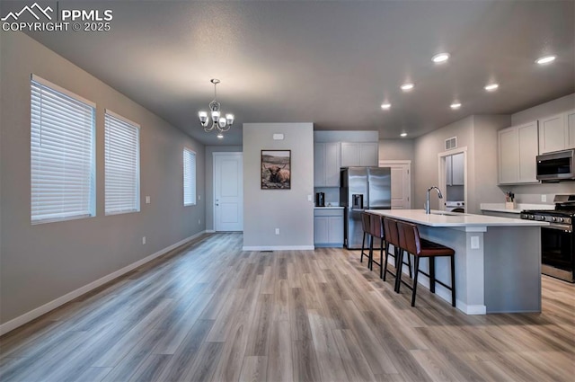 kitchen with stainless steel appliances, light countertops, hanging light fixtures, an island with sink, and baseboards