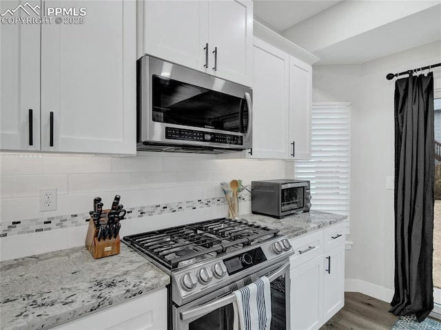 kitchen featuring stainless steel appliances, white cabinetry, backsplash, and light stone counters