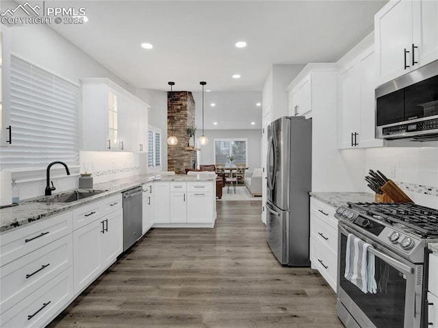 kitchen with appliances with stainless steel finishes, hanging light fixtures, sink, white cabinetry, and kitchen peninsula