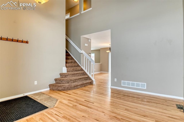 entrance foyer with visible vents, baseboards, stairs, a towering ceiling, and wood finished floors