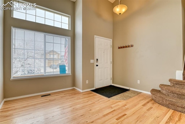 entryway with wood finished floors, visible vents, baseboards, a high ceiling, and stairs