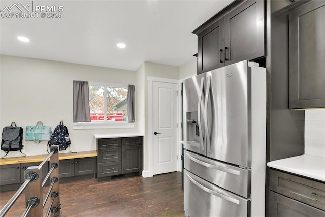 kitchen with dark wood finished floors, built in desk, stainless steel refrigerator with ice dispenser, tasteful backsplash, and light countertops