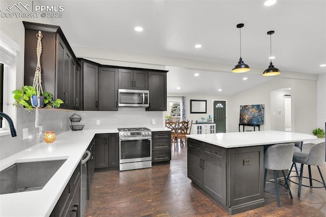 kitchen featuring stainless steel appliances, a sink, light countertops, dark wood finished floors, and pendant lighting