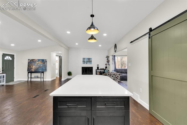 kitchen featuring a barn door, open floor plan, light countertops, dark wood-style floors, and pendant lighting