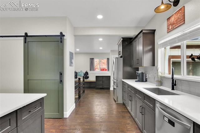 kitchen with a barn door, dark wood-style flooring, a sink, light countertops, and appliances with stainless steel finishes