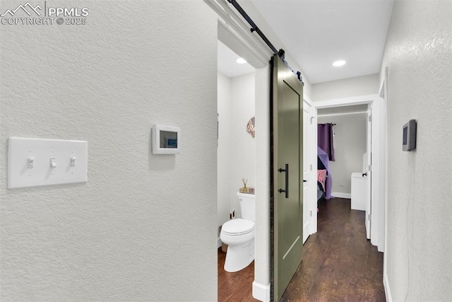 hallway with a barn door, baseboards, wood finished floors, and a textured wall