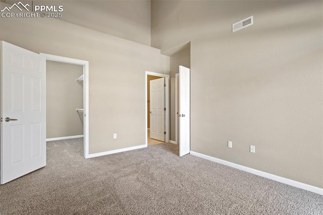 unfurnished bedroom with carpet, visible vents, a spacious closet, and baseboards