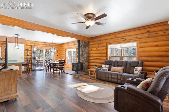 living room featuring a wood stove, ceiling fan with notable chandelier, beamed ceiling, dark hardwood / wood-style floors, and rustic walls