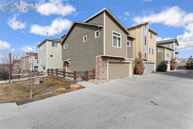 view of property exterior featuring concrete driveway, an attached garage, fence, a residential view, and stone siding