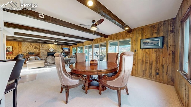 dining room with a fireplace, beamed ceiling, ceiling fan, and wooden walls