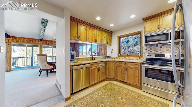 kitchen with stainless steel appliances, light stone counters, decorative backsplash, sink, and light colored carpet