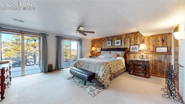 bedroom featuring ceiling fan, access to exterior, light colored carpet, and wooden walls