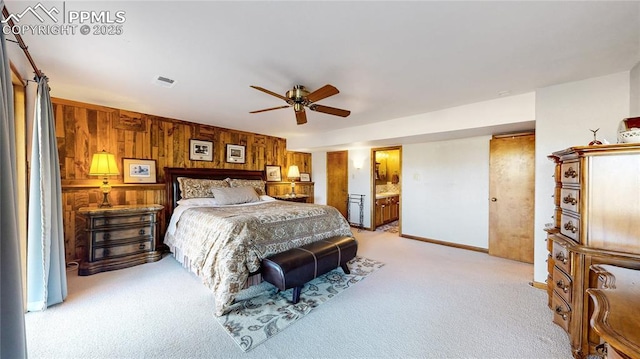 bedroom with ceiling fan, connected bathroom, light colored carpet, and wooden walls