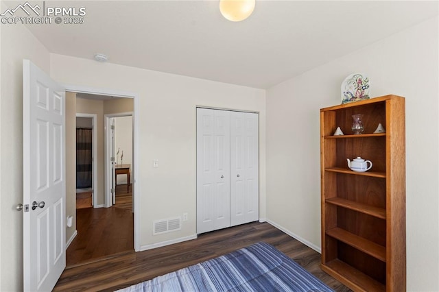 unfurnished bedroom with baseboards, visible vents, dark wood-style flooring, and a closet