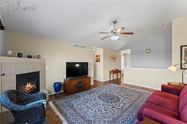 living area featuring a tiled fireplace, visible vents, dark wood finished floors, baseboards, and vaulted ceiling