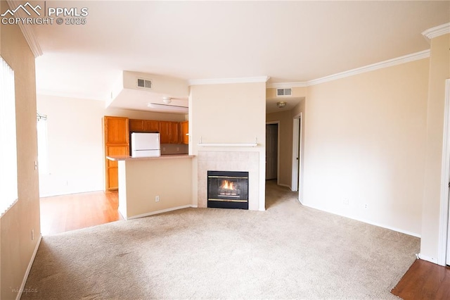 unfurnished living room with ornamental molding, a tile fireplace, visible vents, and light colored carpet