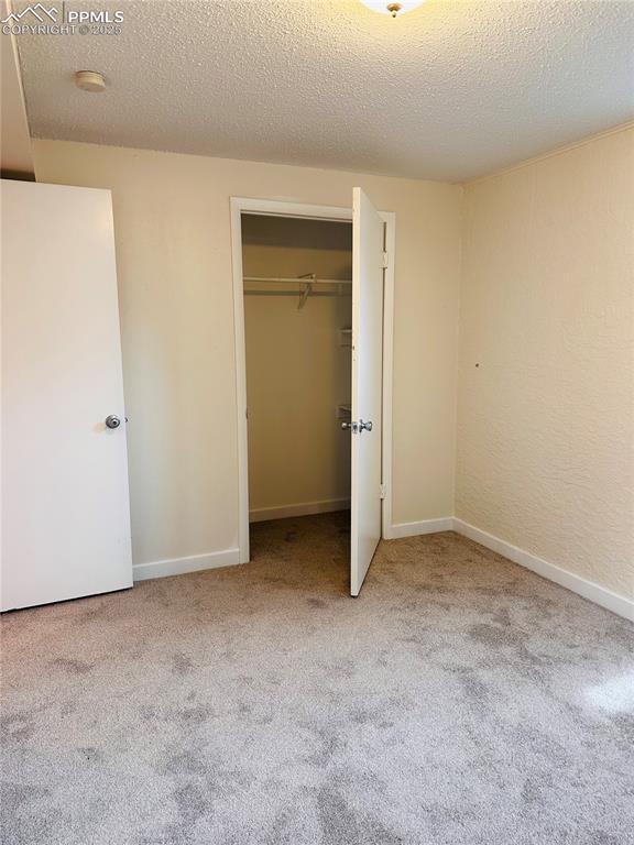 unfurnished bedroom with light colored carpet, a closet, and a textured ceiling