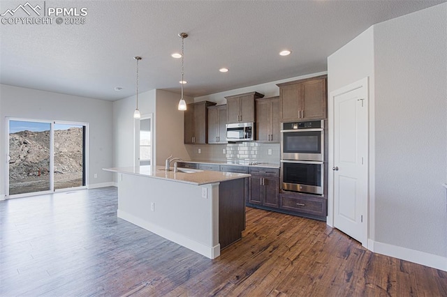 kitchen featuring tasteful backsplash, hanging light fixtures, a center island with sink, dark hardwood / wood-style floors, and stainless steel appliances