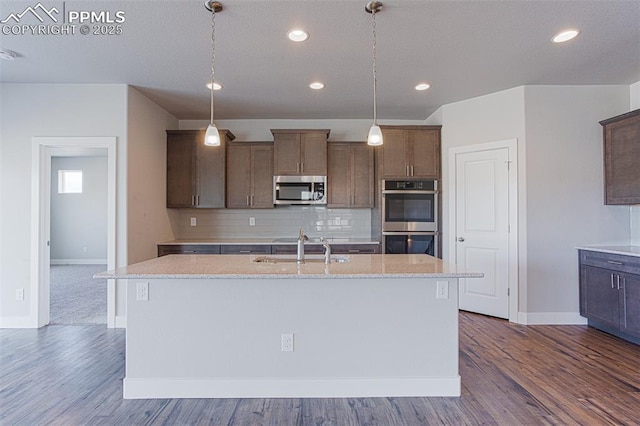 kitchen with light stone counters, stainless steel appliances, and an island with sink