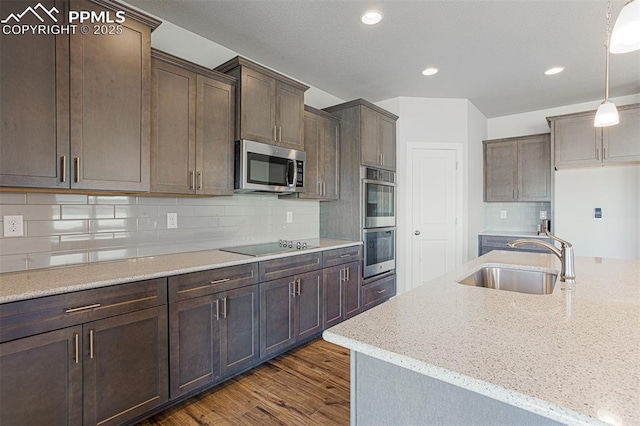 kitchen with hanging light fixtures, appliances with stainless steel finishes, sink, and light stone counters