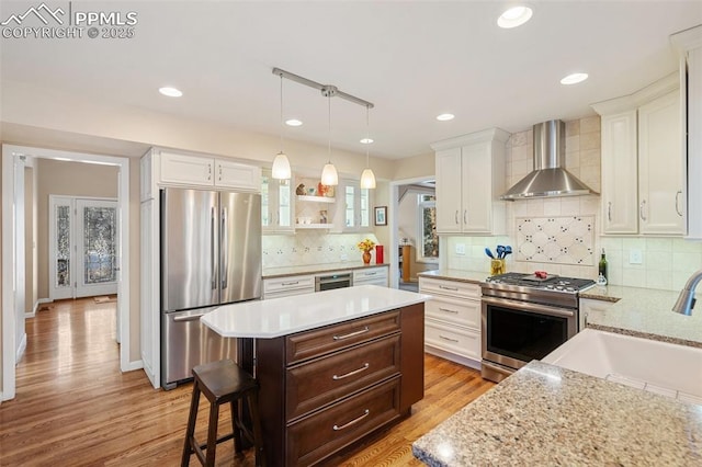 kitchen with appliances with stainless steel finishes, a breakfast bar area, wall chimney exhaust hood, pendant lighting, and white cabinetry