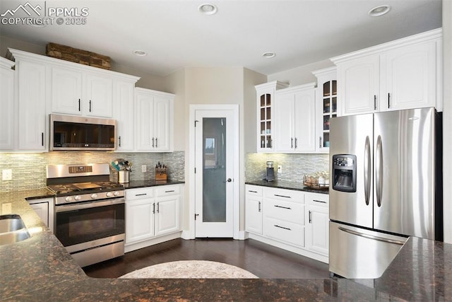 kitchen featuring appliances with stainless steel finishes, dark wood-type flooring, dark stone countertops, white cabinets, and decorative backsplash