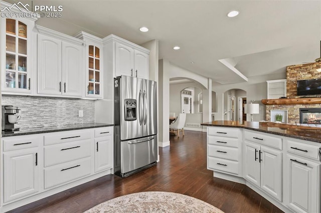 kitchen featuring stainless steel refrigerator with ice dispenser, backsplash, dark stone counters, dark wood-type flooring, and white cabinets