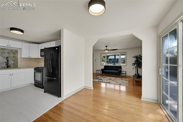 kitchen featuring light wood-style flooring, backsplash, white cabinetry, a sink, and black appliances
