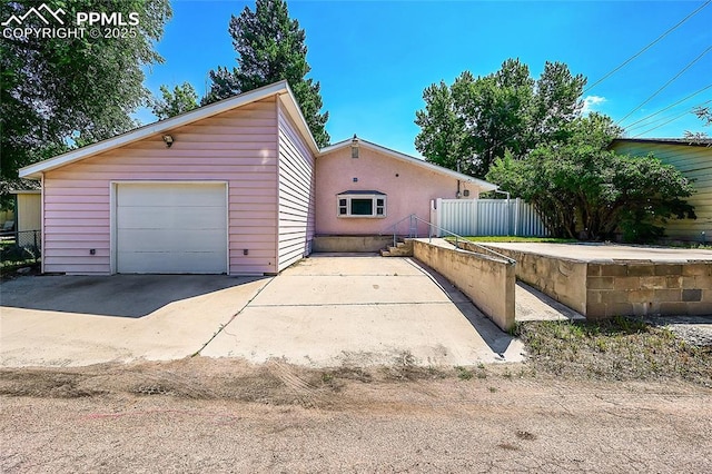 exterior space featuring a garage, fence, driveway, and an outdoor structure