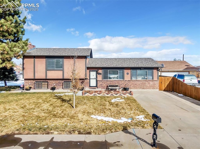 tri-level home featuring brick siding, a front yard, fence, and stucco siding