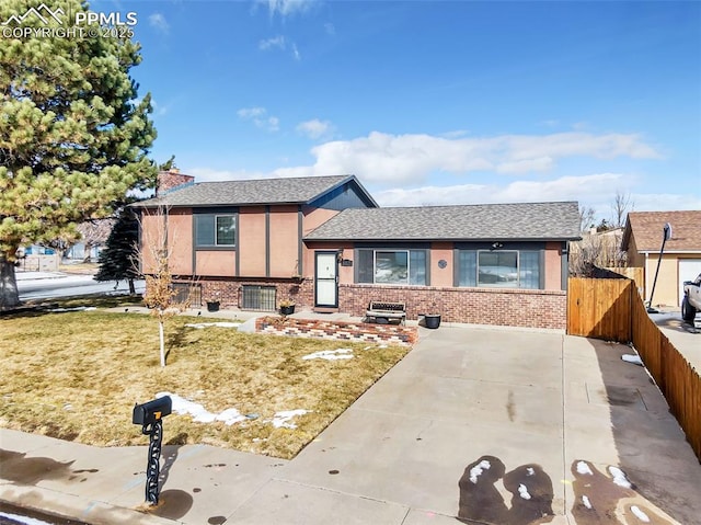 tri-level home featuring brick siding, a shingled roof, fence, a front yard, and stucco siding