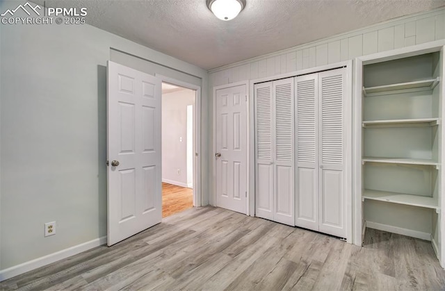 unfurnished bedroom featuring light wood-type flooring, a closet, wooden walls, and a textured ceiling