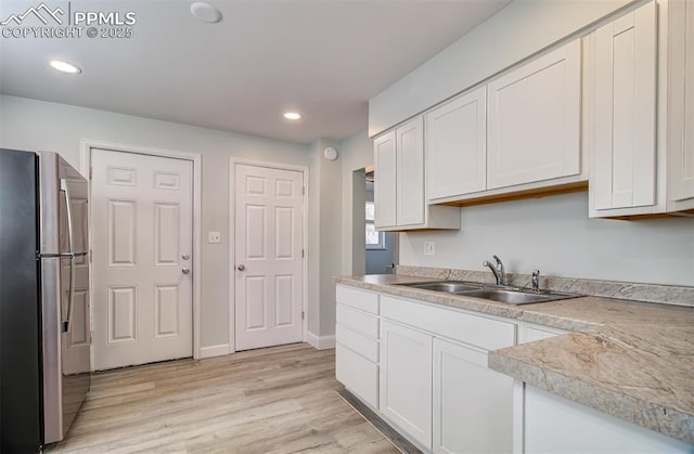 kitchen with stainless steel refrigerator, light hardwood / wood-style floors, sink, and white cabinets