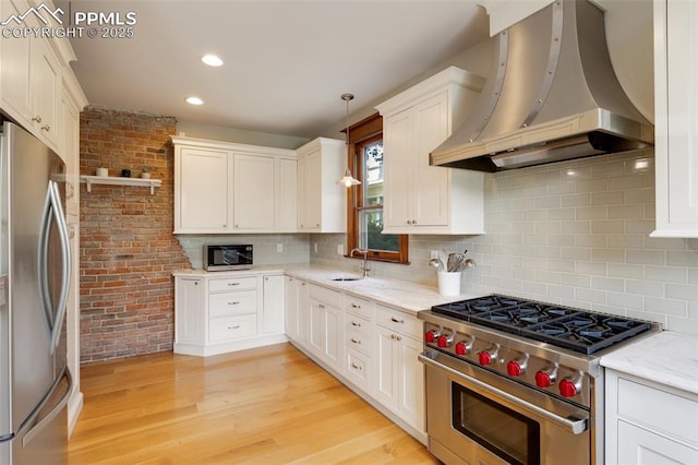 kitchen with stainless steel appliances, light wood-style flooring, a sink, wall chimney range hood, and light stone countertops