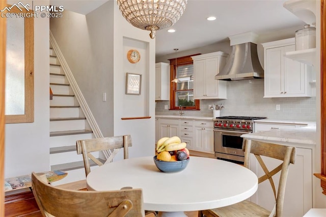 kitchen with designer stove, white cabinets, light countertops, wall chimney exhaust hood, and tasteful backsplash