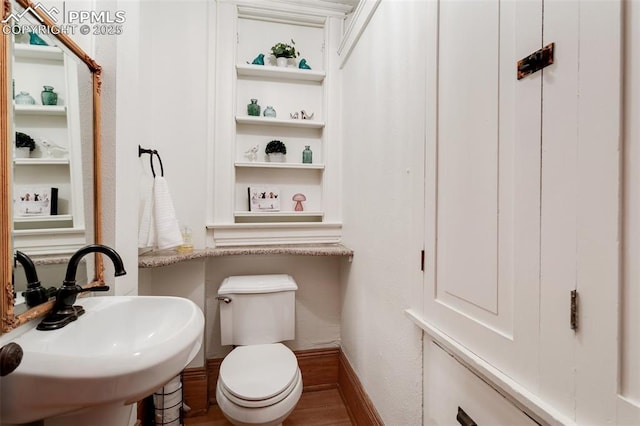 half bath featuring built in features, toilet, a sink, wood finished floors, and baseboards