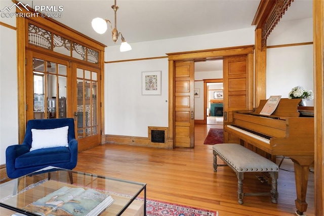 living area with visible vents, baseboards, light wood-style floors, french doors, and an inviting chandelier