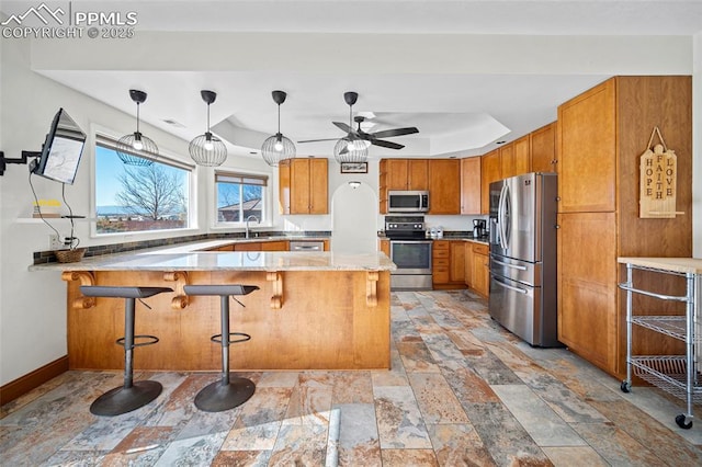 kitchen with a peninsula, a sink, baseboards, appliances with stainless steel finishes, and brown cabinetry