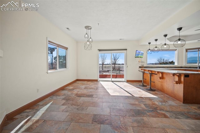 kitchen with stone finish flooring, a breakfast bar, decorative light fixtures, and baseboards