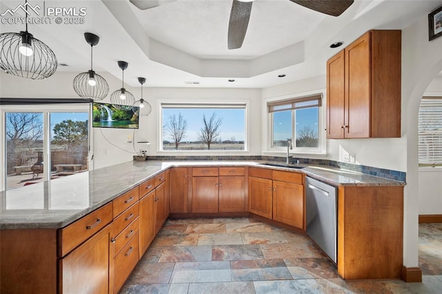 kitchen featuring dishwasher, brown cabinets, dark stone countertops, a peninsula, and a sink