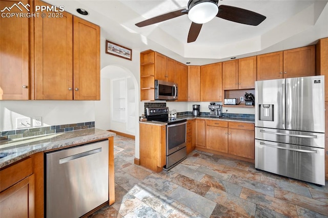 kitchen featuring stainless steel appliances, a tray ceiling, brown cabinets, and open shelves