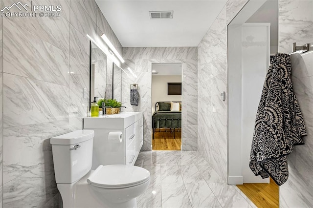 bathroom featuring toilet, ensuite bathroom, visible vents, and tile walls