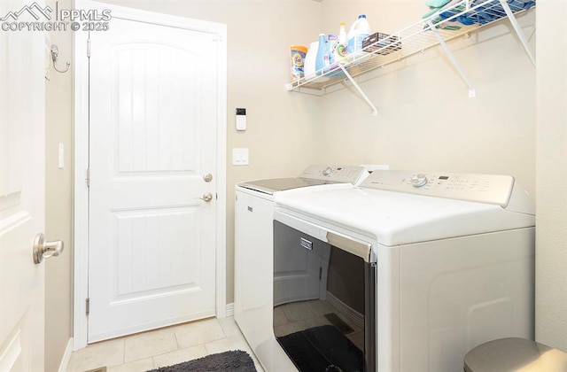 clothes washing area with laundry area, light tile patterned flooring, washer and clothes dryer, and baseboards