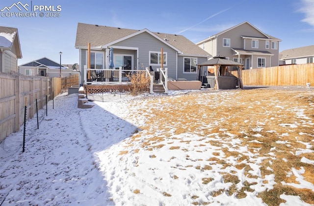 snow covered rear of property featuring a shingled roof, a hot tub, a gazebo, a fenced backyard, and a wooden deck