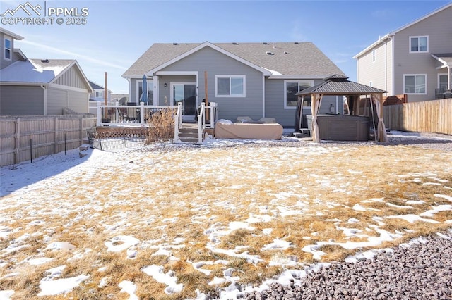 snow covered property with a deck, a fenced backyard, a shingled roof, a gazebo, and a hot tub